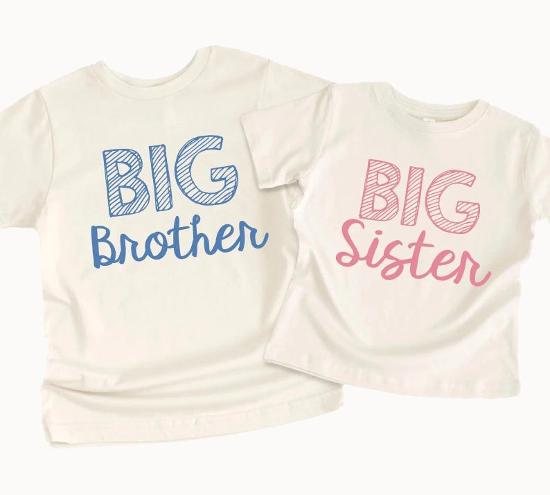 May include: Two off-white t-shirts. One shirt has the words "BIG Brother" in blue, the other has "BIG Sister" in pink. The shirts are likely for children.