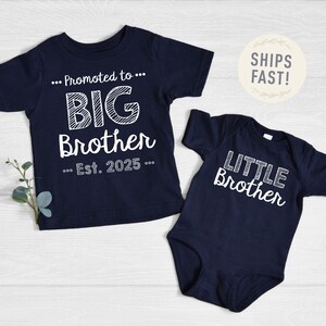 May include: Navy blue t-shirt with "Promoted to BIG Brother Est. 2025" in white text. A navy blue babygrow with "LITTLE Brother" in white text. Both items are baby and toddler apparel.
