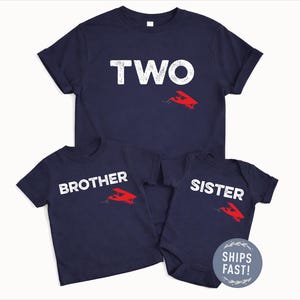 May include: Navy blue t-shirts and a onesie with white text and a red airplane graphic. The shirts say "TWO", "BROTHER", and "SISTER". The onesie has a "SHIPS FAST!" sticker.