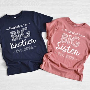 May include: Two t-shirts, one navy blue and one dusty rose, with white text. The navy shirt says "...Promoted to... BIG Brother ...Est. 2026...". The dusty rose shirt says "...Promoted to... BIG Sister ...Est. 2025...".
