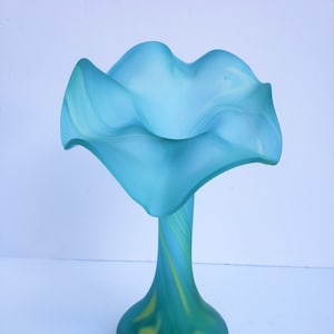 May include: A blue and green glass vase with a wide, ruffled opening and a narrow, curved neck. The vase has a swirl pattern throughout.