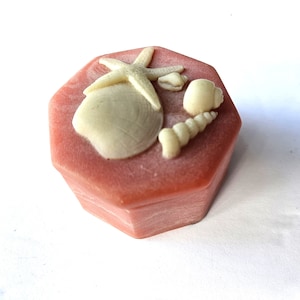 May include: A pink hexagonal trinket box with a raised design of a starfish, seashells, and a conch shell.