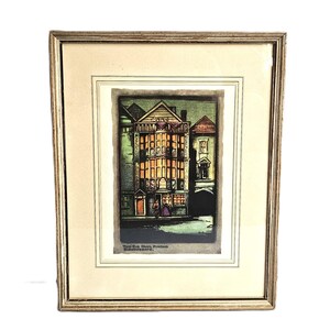 May include: Framed print of a building with a detailed facade, featuring warm interior lighting. The artwork is in a gold-toned frame with a cream-colored mat. The print includes the text "THE SIR PAUL PINDAR, BISHOPSGATE."