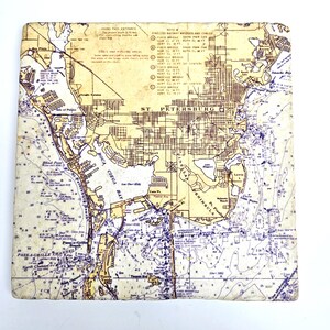 Puede incluir: Un mapa vintage de St. Petersburg, Florida, con fondo beige y líneas azules. El mapa muestra las calles, vías fluviales y puntos de referencia de la ciudad. El texto "St. Petersburg" está impreso en marrón en la parte superior del mapa.