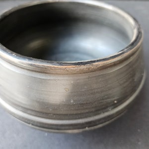 May include: A black ceramic bowl with a rounded shape and a slightly flared rim. The bowl has a smooth, glossy finish.