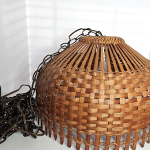 May include: A woven brown pendant light fixture with a rounded shade and a chain for hanging. The shade is made of woven bamboo strips and has a textured appearance. The light fixture is designed for indoor use.