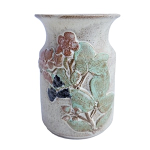 May include: A beige ceramic vase with a textured surface. The vase features a raised floral design in shades of brown, blue, and green. The vase has a wide body and a slightly flared rim, suitable for displaying flowers or as a decorative piece.
