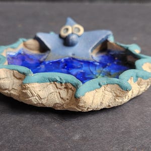 Puede incluir: Un plato de cerámica hecho a mano con un diseño de estrella de mar. El plato presenta una estrella de mar azul en el centro, rodeada de un diseño de agua azul y blanco. El borde es de color beige claro con un borde turquesa.