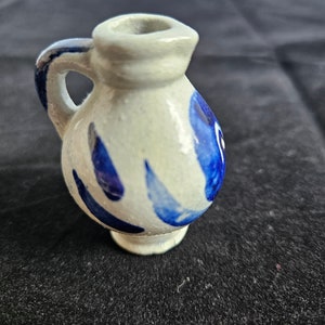Könnte beinhalten: Ein kleiner weißer Keramik Krug mit blau-weißem Design. Der Krug hat einen Henkel und einen runden Körper.