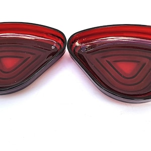 May include: Two red glass dishes with a triangular shape and a layered design. The dishes have a glossy finish and are set against a white background. These decorative dishes are suitable for serving snacks or as decorative pieces.