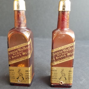 May include: Two miniature glass bottles with gold labels and silver tops. The labels read "Johnnie Walker Red Label Old Scotch Whisky".