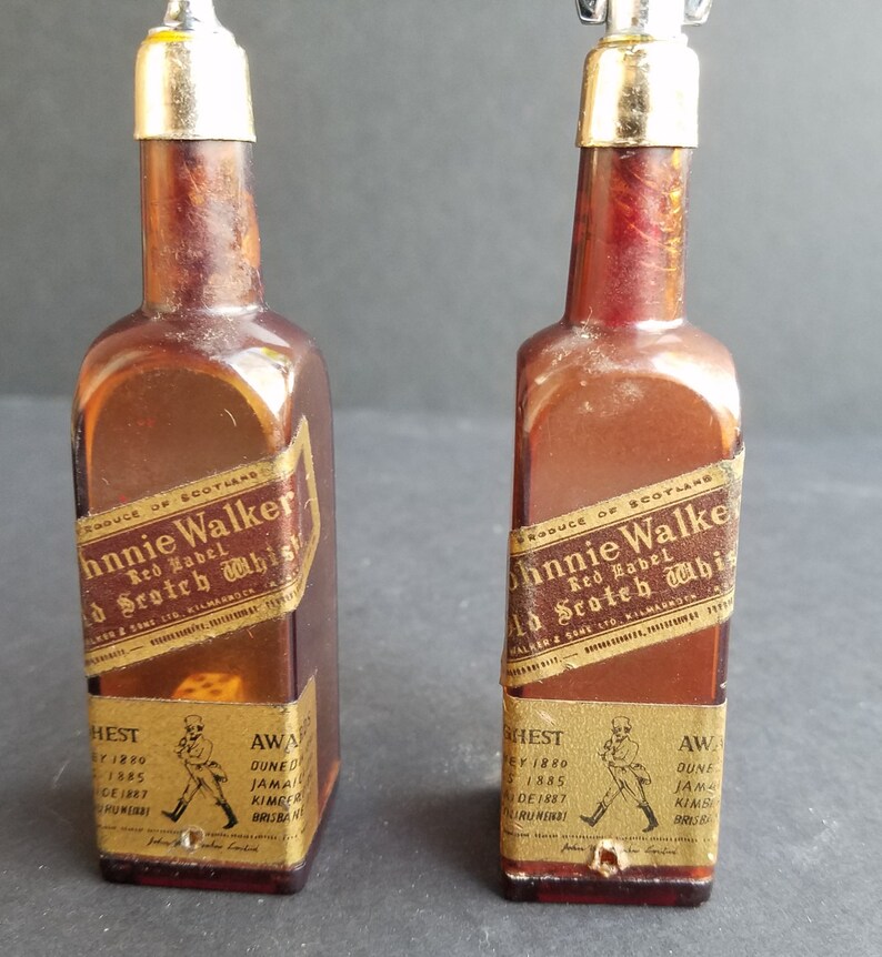 May include: Two miniature glass bottles with gold labels and silver tops. The labels read "Johnnie Walker Red Label Old Scotch Whisky".