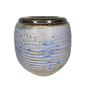 Peut inclure: Un vase en céramique arrondi présentant une surface texturée et nervurée avec un émail bleu et gris. Le bord supérieur est fini dans un ton brun foncé brillant, tandis que le corps affiche des stries horizontales et des variations de couleur.