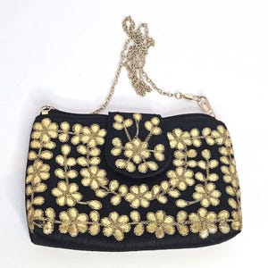 May include: Black clutch with gold floral embroidery and a silver chain strap. The rectangular bag features a flap closure and a zipper. The gold embroidery is in the shape of flowers.