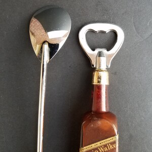 May include: A silver bottle opener and a silver spoon with a long handle. The bottle opener has a brown wooden handle with the text "PRODUCE OF SCOTLAND" and "WALKER" printed on it.