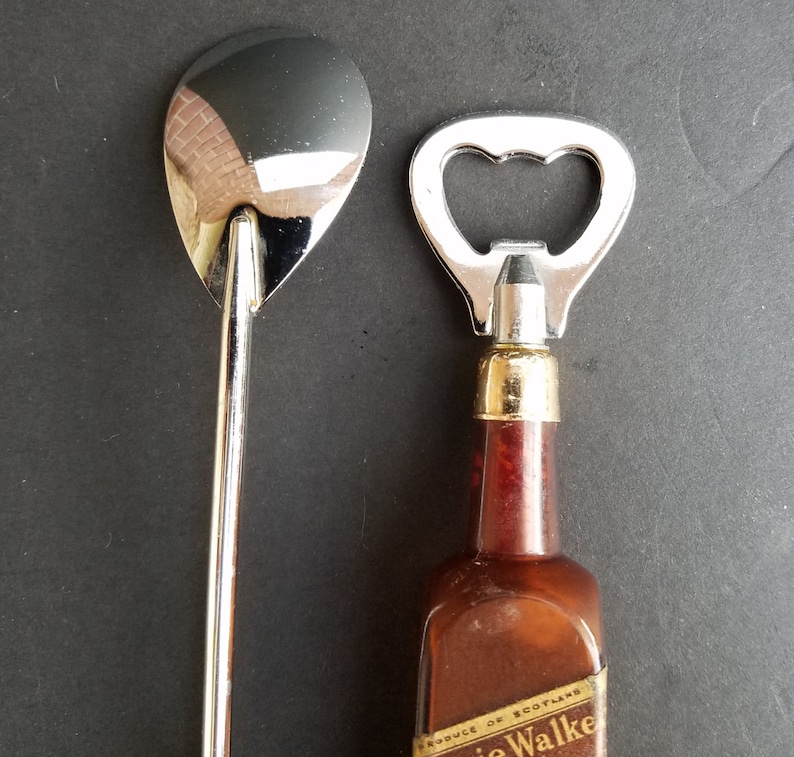 May include: A silver bottle opener and a silver spoon with a long handle. The bottle opener has a brown wooden handle with the text "PRODUCE OF SCOTLAND" and "WALKER" printed on it.