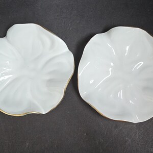 May include: Two white, petal-shaped ceramic dishes with a gold trim. The dishes have a glossy finish and a delicate, organic design. These decorative dishes are ideal for serving small portions or as decorative accents.