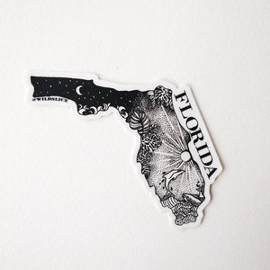 May include: Black and white sticker of the state of Florida with a sun, moon, and ocean waves design. The sticker says "WILD SLICE" and "FLORIDA".