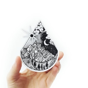 May include: Black and white sticker of a mountain range with a sun and moon in the sky. The sticker is shaped like a teardrop.