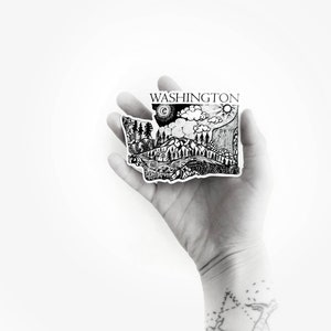 May include: Black and white sticker of the state of Washington with a detailed illustration of mountains, trees, a river, and a sun and moon in the sky. The sticker says "WASHINGTON" at the top.