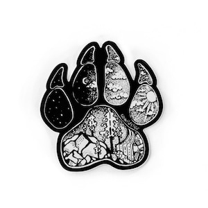 May include: Black and white sticker of a paw print with a detailed illustration of a forest scene inside. The paw print is outlined in black and the forest scene is filled with white details. The text "@wildslice" is visible in the lower right corner of the sticker.