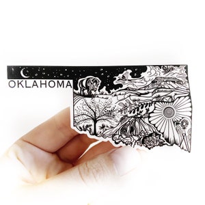 May include: Black and white line art sticker of the state of Oklahoma with various illustrations including a bison, a tree, a sunflower, and a windmill. The sticker has the word "OKLAHOMA" printed at the top.