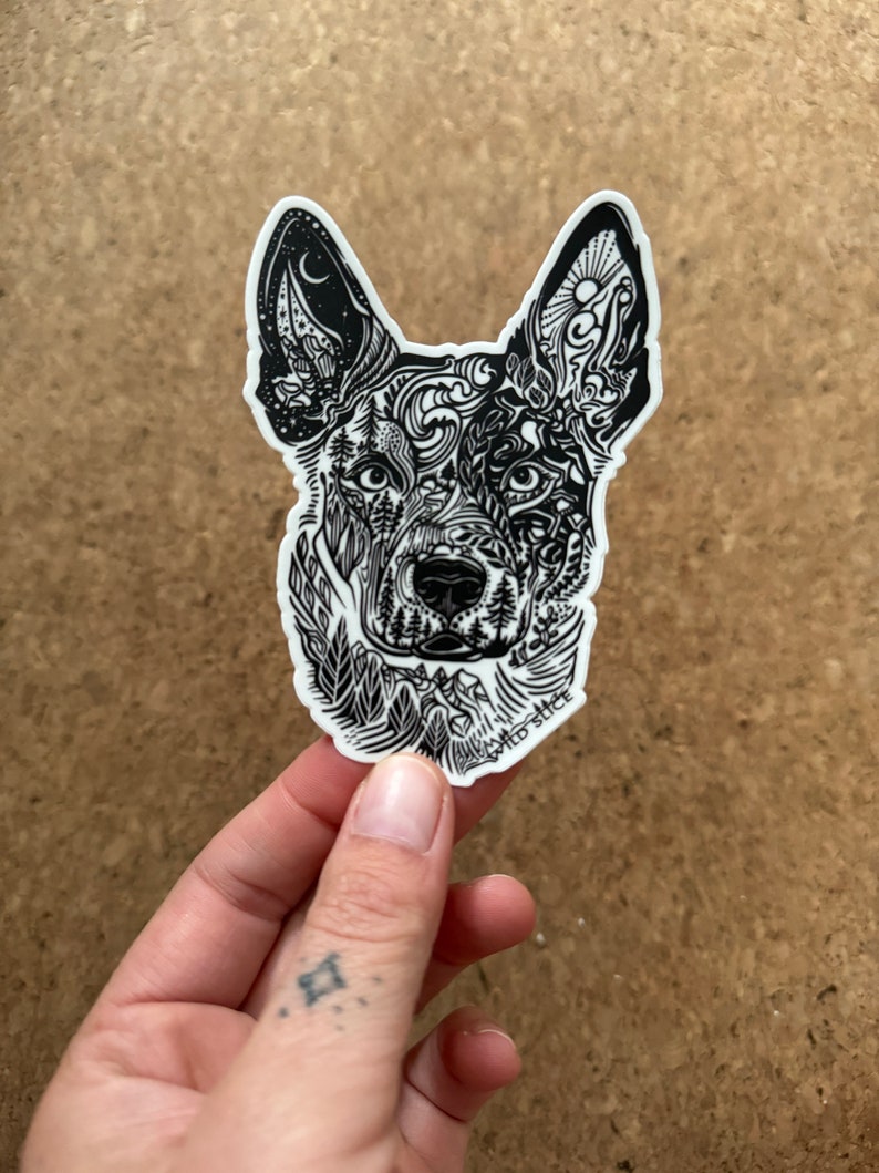 K&ouml;nnte beinhalten: Schwarz-wei&szlig;er Aufkleber mit dem Kopf eines Hundes mit komplizierten Linienkunstdesigns. Der Kopf des Hundes ist mit naturinspirierten Mustern gef&uuml;llt, darunter B&auml;ume, Berge und Sterne. Der Aufkleber befindet sich auf einem wei&szlig;en Hintergrund.