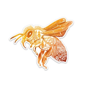 May include: A gold and orange bee sticker with intricate details, including a forest, honeycomb, and flowers. The bee is in flight and has a stylised design. The sticker has the text "@WILD.SLICE" on the bottom.