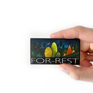 May include: A black and white sticker featuring a stylised illustration of a forest scene at night. The sticker has the text "FOR-REST" in white lettering.