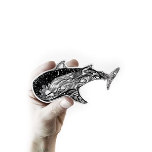 May include: A black and white sticker of a whale with intricate details, including waves, stars, and a sun. The whale is swimming towards the right side of the image.