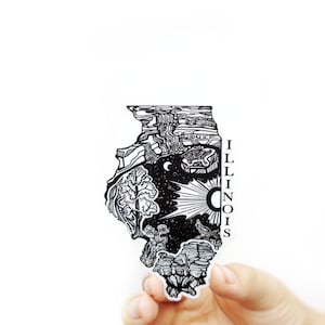 May include: Black and white sticker of the state of Illinois with a detailed illustration of the state's landscape and the word "ILLINOIS" written vertically on the right side. The sticker is held in a hand.