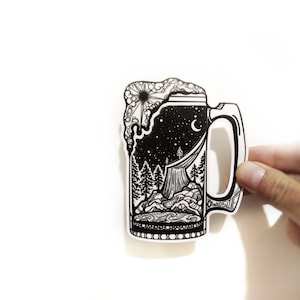 May include: Black and white illustration of a beer stein with a night sky, stars, moon, and a mountain scene inside. The stein has a handle and a foamy top.