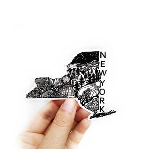 May include: A black and white sticker in the shape of New York State, with detailed illustrations of landscapes and landmarks. The word "NEW YORK" is printed vertically on the right side of the sticker.