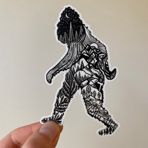 May include: Black and white sticker of a Bigfoot walking with a forest scene inside its body. The text "Wild Slice" is on the bottom of the sticker.