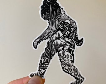 May include: Black and white sticker of a Bigfoot walking with a forest scene inside its body. The text "Wild Slice" is on the bottom of the sticker.