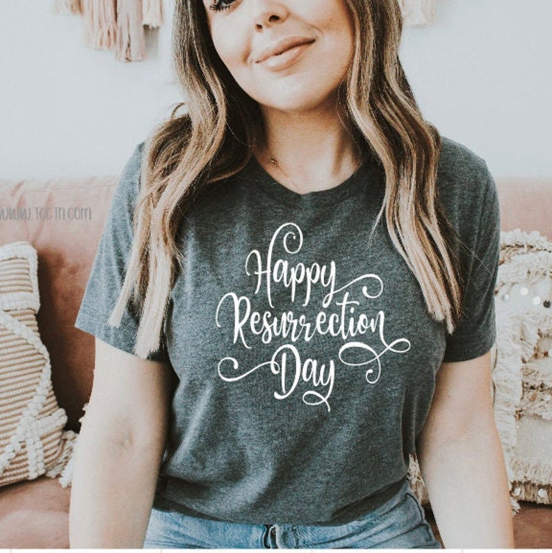 May include: Dark gray t-shirt with a v-neck and the words "Happy Resurrection Day" in white script. The shirt is a short-sleeved tee. The text is in a cursive font.