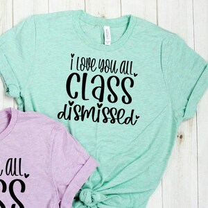 May include: Two light green and light purple t-shirts with black text. The light green t-shirt says "I love you all. Class dismissed." The light purple t-shirt says "I love you all. Ass."