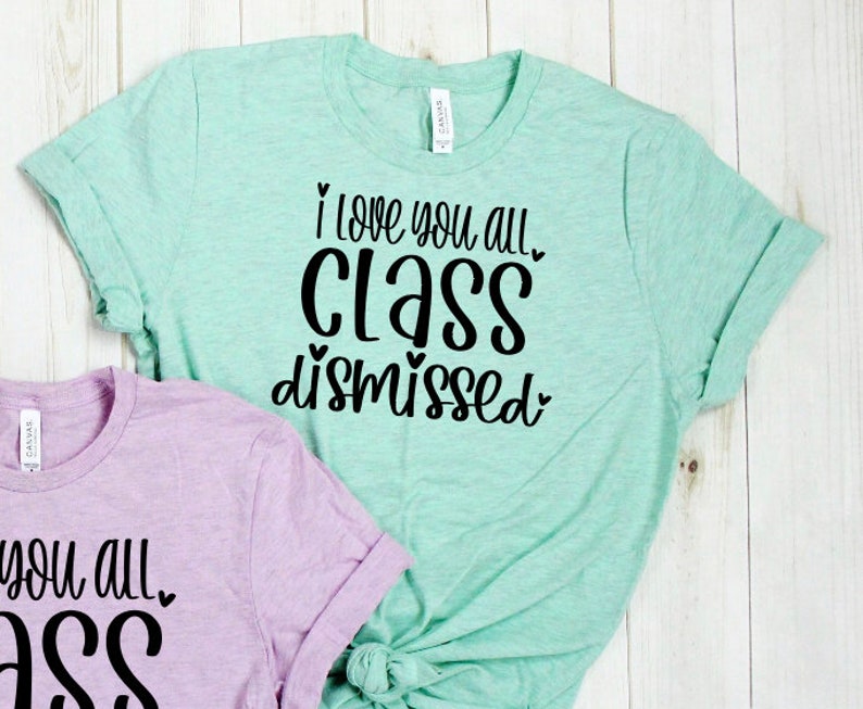 May include: Two light green and light purple t-shirts with black text. The light green t-shirt says "I love you all. Class dismissed." The light purple t-shirt says "I love you all. Ass."