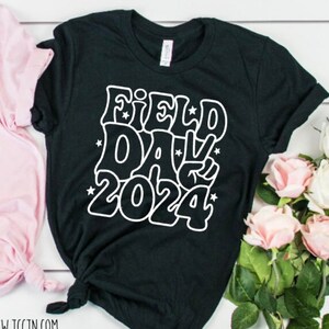 May include: Black t-shirt with white text that says "Field Day 2024" in a retro font with stars.
