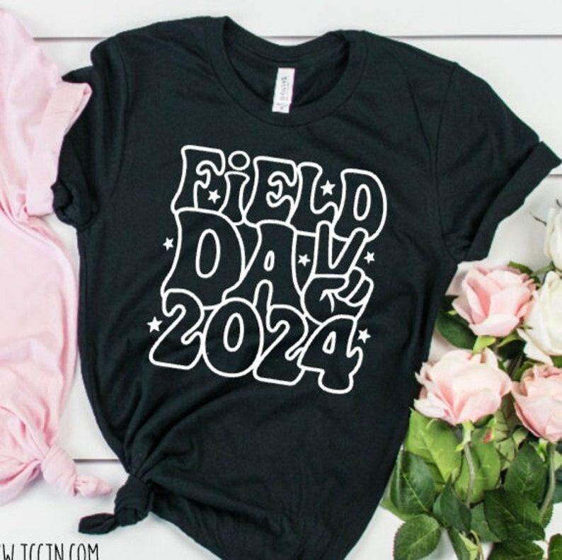 May include: Black t-shirt with white text that says "Field Day 2024" in a retro font with stars.