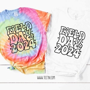 May include: Two t-shirts with a tie-dye design and a white design. Both shirts feature a black graphic that says "Field Day 2024" in a retro font with stars.