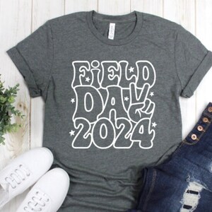 May include: A dark gray t-shirt with a white graphic design that says "Field Day 2024" in a retro font with a peace sign.
