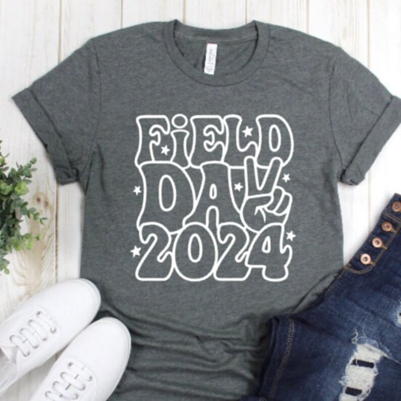 May include: A dark gray t-shirt with a white graphic design that says "Field Day 2024" in a retro font with a peace sign.