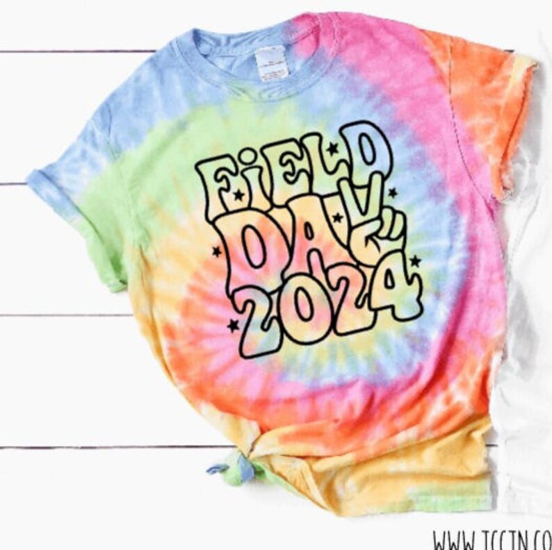 May include: A tie-dye t-shirt with a rainbow swirl pattern. The shirt has a black outline of the text "FIELD DAY 2024" in a retro font.