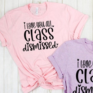 May include: Two pink and purple t-shirts with black text that reads "I love you all class dismissed" with hearts around the words.
