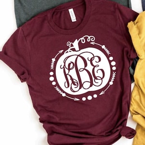 May include: A maroon t-shirt with a white pumpkin design. The pumpkin has a monogram inside of it that says "KBE".