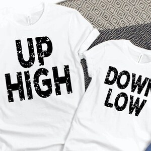 May include: Two white t-shirts with black text. The first t-shirt says 'UP HIGH' and the second t-shirt says 'DOWN LOW'.