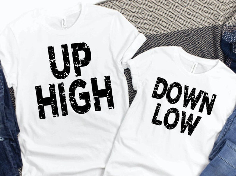 May include: Two white t-shirts with black text. The first t-shirt says 'UP HIGH' and the second t-shirt says 'DOWN LOW'.