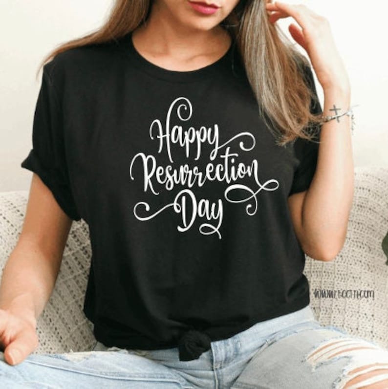 May include: Black t-shirt with the white text "Happy Resurrection Day" in a cursive font. The shirt is a crew neck and has short sleeves. The shirt is tied at the waist.