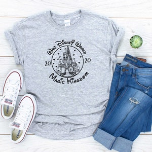May include: A gray t-shirt with a black and white graphic of Cinderella's castle in a circle with the text "Walt Disney World 2020 Magic Kingdom".